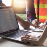 Handwerker in Arbeitskleidung planen gemeinsam ein Projekt am Tisch, mit geöffnetem Laptop im Vordergrund – Digitalisierung im Handwerksbetrieb