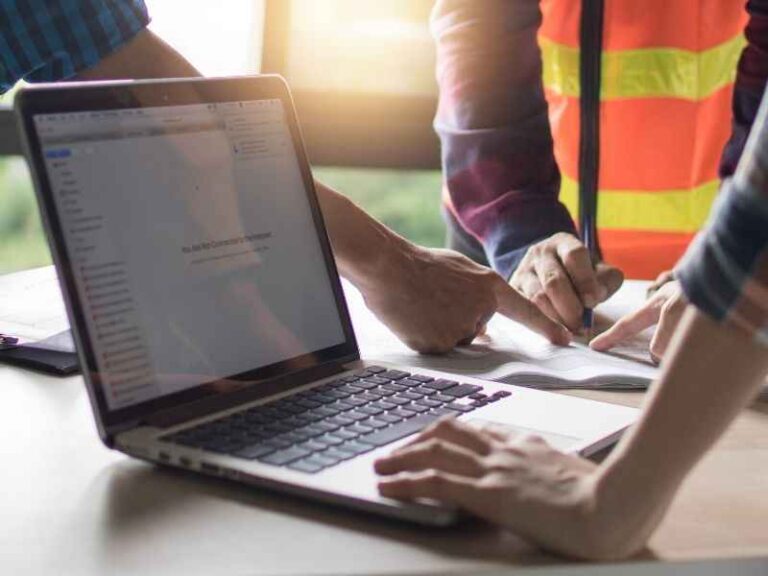 Handwerker in Arbeitskleidung planen gemeinsam ein Projekt am Tisch, mit geöffnetem Laptop im Vordergrund – Digitalisierung im Handwerksbetrieb